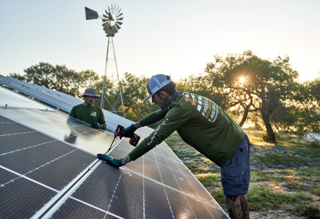 Arbeiter bohrt bei Sonnenuntergang Solarpanel zur Bodenmontage