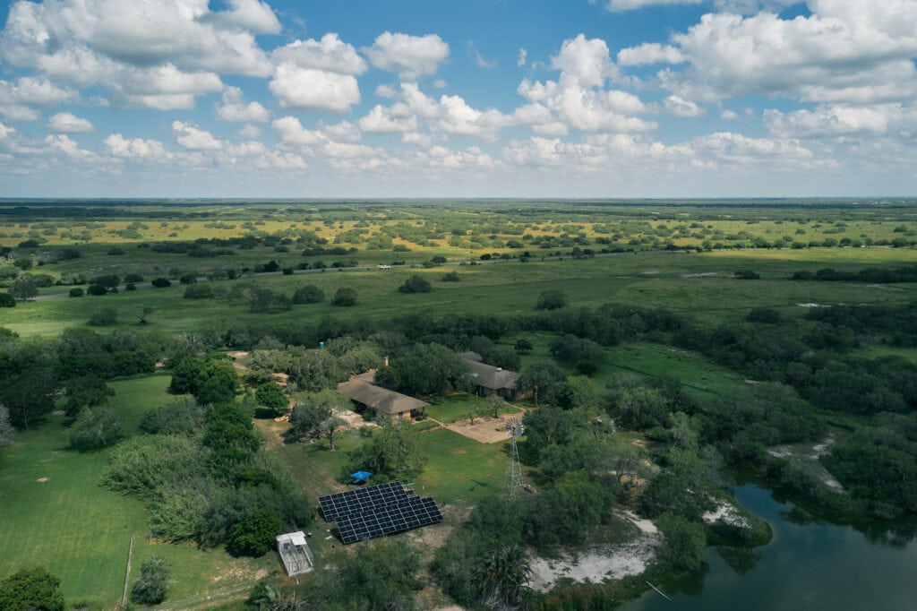 Luftaufnahme eines Ranchhauses, bodenmontierter Sonnenkollektoren und der grünen Küstenwiesen von Texas